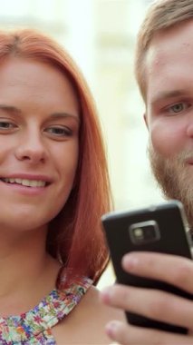 Canlı genç bir çift, saf neşe saçıyor, güneş ışığında bir bankta, akıllı telefonlarıyla enfes bir selfie çekiyorlar. Onların neşeli ifadeleri ve sıcak gülümsemeleri kaygısız bir yaz gününün özünü özetliyor, izleyicileri katılmaya davet ediyor.