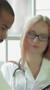 Parlak, modern bir klinikte, kendini adamış bir doktor ve bir hasta zarif bir tabletin tıbbi sonuçlarını incelerken düşünceli bir tartışmaya girişirler. Steteskopla süslenmiş özenli doktor profesyonellik ve şefkat yayıyor.