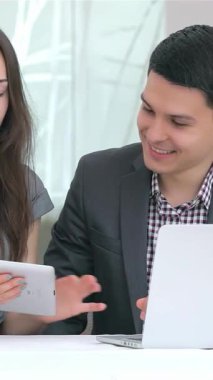 Canlı genç bir iş adamı ve kadın, parlak, modern bir ofis zeminine karşı hazırlanan parlak bir tablet üzerindeki verileri analiz ederken hareketli bir tartışmaya girişiyor. Onların coşkulu ifadeleri ve işbirlikçi enerjileri yenilik ruhunu somutlaştırıyor.