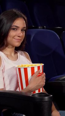 Işıl ışıl genç bir kadın loş bir sinema sandalyesinde otururken klasik çizgili patlamış mısır kovasını tutarak zevkle ışıldıyor. Bu canlı sahne, sinema gecelerinin heyecanını özetliyor. Seyircileri, sinemanın zevkine ve heyecanına davet ediyor.