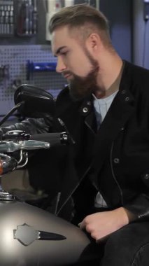 Çarpıcı bir beyaz erkek motorcu motosiklet gidonunu sıkıca kavrıyor, parlak siyah deri ceketiyle serinlik yayıyor. Bu genç sakallı adam parlak bir motorsiklet içinde parıldayan aletler ve makinelerle çevrili parlak bir helikopterde oturuyor.