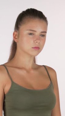 Uzun, dalgalı saçları olan yeşil kolsuz bir bluz giyen genç bir kadın dirseğini görünür bir sıkıntı içinde sallarken kameraya dikkatle bakıyor. Bu çarpıcı görüntü onun duygusal mücadelesini ve kararlılığını özetliyor.