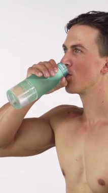 Formda ve yakışıklı bir adam, güçlü bir egzersizden sonra serin bir şişeden gelen soğuk suyla kendini serinletirken parlak bir gülümseme sergiliyor. Bu dinamik sahne sağlık ve zindelik yayıyor, hidratlaşmanın önemli rolünü vurguluyor.