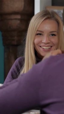 Büyüleyici bir kafede, neşeli bir kadın erkek arkadaşına şakacı bir şekilde dilini uzatıyor, elinde sahneye biraz sıcaklık katan beyaz bir bardak tutuyor. Onun ışıl ışıl gülüşü ve sıradan mor süveteri davetkar bir atmosfer yaratırken, erkek arkadaşı...