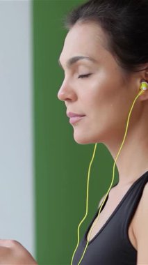 Neşeli genç bir kadın yoga yapıyor, parlak sarı kulaklıklarıyla neşeli müzik dinlerken zarifçe geriniyor. Bu canlı sahne pozitifliği ve refahı yansıtıyor. Renkli vücudunu parlak siyah bir elbiseyle vurguluyor.