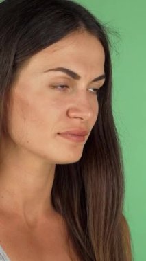 Uçan esmer saçlı güzel genç bir kadın berrak bir bardak sudan ferahlatıcı bir yudum alır, neşe ve canlılık saçar. Canlı yeşil bir arka plan karşısında, kendine güveni ve sakin ifadesi sağlığın özünü yakalar.