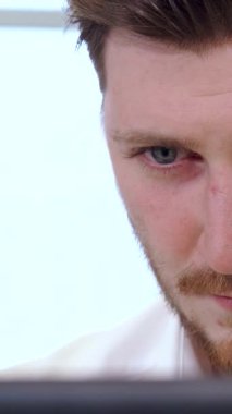 Yakışıklı, genç, beyaz bir erkek yöneticinin çarpıcı yakın çekimi, şık bir sakalı var, dizüstü bilgisayarına dalmış, şık, modern bir ofiste. Yumuşak doğal ışık pencereden akar, ciddi yüz ifadesine sıcak bir parıltı yayar,