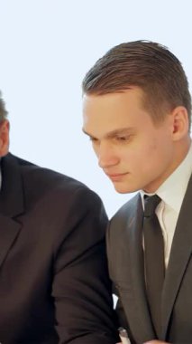 İki keskin giyimli adam, biri ciddi davranışlı diğeri dikkatle odaklanmış, düzgün bir dizüstü bilgisayar üzerinde işbirliği yaparak önemli verileri analiz ediyorlar. Bağlı ifadeleri ve yakın yakınlıkları, takım çalışmasının ve stratejik planlamanın özünü vurgular.