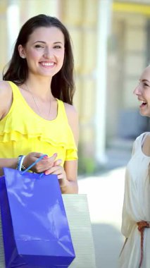 İki ışıl ışıl kız, biri güneşli sarı elbiseli, diğeri şık beyaz elbiseli, canlı bir arkadaş grubunun arasında canlı alışveriş torbalarını gururla sergiliyorlar. Bulaşıcı gülümsemeleri ve kaygısız tavırları alışverişin heyecanını ve...