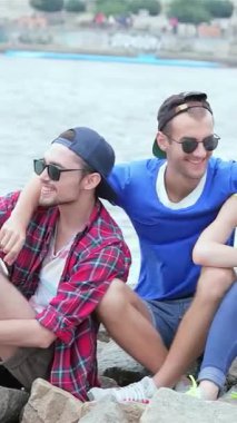 Üç genç arkadaş ılık yaz güneşinin tadını çıkarıyor, nehri seyrederken neşe dolu anlar ve kahkahalar atıyorlar. Kaygısız gülümsemeleri ve rahatlamış pozları, bu güzel havada unutulmaz anılar yaratarak dostluk ruhunu somutlaştırıyor.