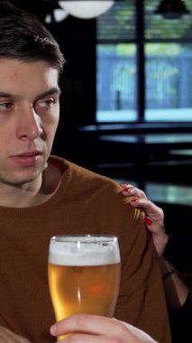 Sıcak bir bar ortamında, genç bir adam etrafını saran arkadaşları kahkaha ve destekle dolu kadehlerini kaldırırken dalgın bir şekilde görünür. Bu canlı sahne arkadaşlığın sıcaklığını güzel bir şekilde gösteriyor, canlandırıcı gücü vurguluyor.