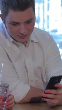 Çekici beyaz bir adam ve genç bir esmer kadın, şık bir kafede gülüşlerini ve bağlantılarını paylaşan bir akıllı telefondan etkileniyorlar. Zinde olan beyaz gömlekli adam, elinde parlak siyah bir telefon tutarken, kadın ferahlatıcı bir kokteylin tadını çıkarıyor.