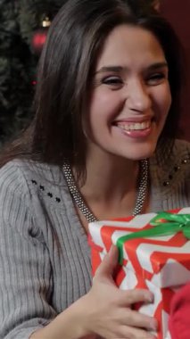 Işıl ışıl beyaz bir kadın, kızı ona parıldayan ışıklar ve şenlikli bir ağaçla süslenmiş rahat bir oturma odasıyla sarılı muhteşem bir Noel hediyesi verirken neşeyle parlıyor. Bu iç açıcı sahne tatilin özünü yansıtıyor.