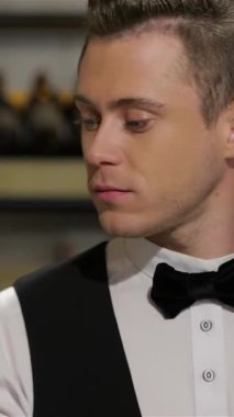 Şık bir elbise giymiş genç, çekici bir şarap garsonu gururla sunar. Sıcak bir gülümseme, sofistike ve uzmanlık dolu bir şarap şişesi. Bu davetkar sahne lüks ve şarap tatma sevinci ile müşterileri cezbediyor.