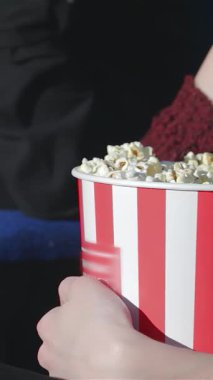Canlı kırmızı ve beyaz çizgili patlamış mısırı kavrayan ve film gecesinin heyecanını yayan bir elin yakın çekimi. Arkadaşları neşe ve neşe içinde, keyifli bir film deneyimine dalarken lezzetli atıştırmalıkları paylaşıyorlar.