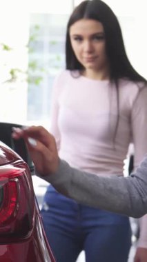 Canlı bir galeride, iki kadın, biri çarpan kırmızı bir arabanın parlak arkasını nazikçe okşarken, arkadaşı keskin bir ilgiyle izlerken neşeli bir anı paylaşıyor. Bu canlı sahne güven ve dostluğu yansıtıyor, heyecanı yakalıyor.