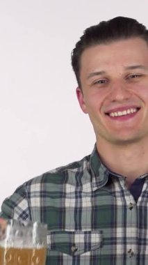 Yakışıklı, neşeli genç bir adam gururla elinde köpüklü bir bira bardağıyla sizi lezzetli bir krakerin yanında anın tadını çıkarmaya davet ederken neşe saçıyor. Canlı gülüşü ve şık ekose gömleği enerjik bir atmosfer yaratıyor, şenlik için mükemmel.