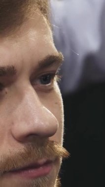 Bu büyüleyici yakın plan, saçlarını titizlikle kesen yetenekli bir berber gibi düşüncelere dalmış çarpıcı mavi gözlü genç bir adamı gösteriyor. Berber dükkanının canlı atmosferi tımar etme sanatını geliştiriyor, modern stilin bir karışımını sergiliyor ve