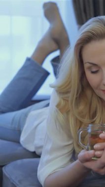 Sevimli beyaz bir kadın karnı üzerinde dinleniyor, pelüş gri bir kanepeye kurulmuş, dumanı tüten bir fincan çayı nazikçe kucaklıyor. Huzurlu gülüşü ve samimi çevresi huzur ve rahatlık hissi uyandırıyor. Seyircileri yanında dinlenmeye çağırıyor.