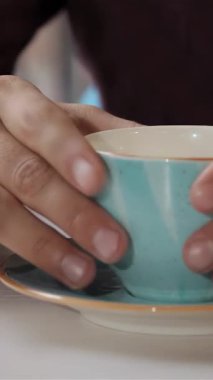 Yakın plan çekimde bir çift erkek eli zarif mavi kahve fincanını el değmemiş dairesinden kaldırıyor. Bu davetkar sahne sıcaklığı ve konforu yayar, cazip kahve meraklılarını zengin aromaları ve enfes lezzetleriyle şımartır.