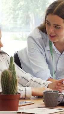 Parlak ve modern bir çalışma alanında, şık genç bir bayan tasarımcı asistanıyla iş birliği yaparak bir dizüstü bilgisayarla fikirleri paylaşıyor. Canlı malzemeler ve rahat bir atmosferle çevrelenmiş bu dinamik ikili, yaratıcılığı ve modada takım çalışmasını somutlaştırıyor.