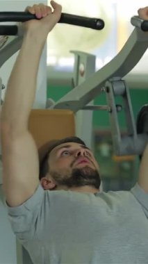 Orta Doğu kökenli odaklanmış genç bir adam göğüs kası egzersizleriyle yoğun bir şekilde meşgul, sarsılmaz bir kararlılıkla ağırlık kaldırıyor. Spor salonları onu çevreleyen enerjik enerji, onun heykeltraş fiziğinin altını çiziyor ve kendini adamışlığını gösteriyor.