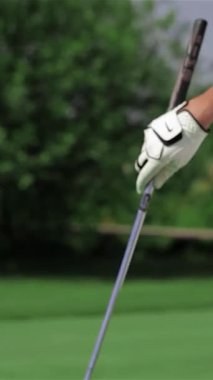 Şık bir golf kıyafeti giymiş kararlı, genç, kızıl saçlı bir kadının yakın plan fotoğrafı. Parlak yeşil bir sahada golf sopasını ustalıkla topa doğrultuyor. Kırmızı ayakkabılarla vurgulanan atletik duruşu yaz sporlarının ve