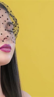 Zarif bir Asyalı kadın zarif bir şekilde siyah bir peçe ile örtülmüş, büyüleyici gözlerini kapatıyor ve canlı sarı bir zemin üzerinde derin derin nefes alıyor. Bu büyüleyici portre entelektüellik ve çekicilik yayıyor. Kusursuz cildini vurguluyor.