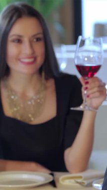 Çekici genç bir çift romantik bir anı paylaşıyor, kırmızı şarap kadehlerini neşe içinde kaldırırken garsonu çağırıyorlar. Yumuşak ışıklandırma ve narin güllerle süslenmiş zarif restoran, özel bir ortam yaratıyor.