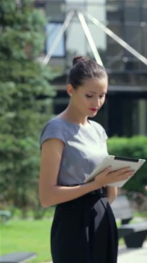 Şık gri bir bluz ve özel dikim siyah pantolon giyen dengeli bir iş kadını, tabletindeki verileri dikkatle inceleyerek güven ve profesyonellik yayıyor. Canlı bir şehir zeminiyle çevrelenmiş, modern liderliğin özünü somutlaştırıyor ve...