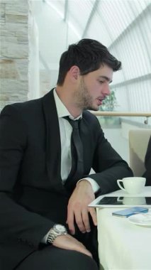 Gösterişli siyah takım elbiseli şık giyinmiş bir adam, meslektaşlarıyla çevrili canlı bir iş toplantısına katılıyor. Modern ofis ortamı, parlak, havadar atmosferiyle, yenilikçi paylaşımları ile işbirlikçi ruhu geliştirir.