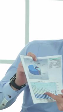 Parlak, güneşli bir ofiste, açık mavi gömlekli kendine güvenen bir işadamı, nişanlı meslektaşına coşkulu grafikler sergiliyor. Hava, başarı için strateji oluşturan, modern dünya ile çevrelenmiş, işbirliği ve hırsla dolu.