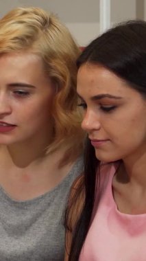 İki hayat dolu genç kadın, biri dalgalı sarı saçlı ve diğeri parlak koyu saçlı, neşeli bir şekilde bir dizüstü bilgisayarda iş birliği yapıyorlar, kahkahaları parlak, modern bir çalışma alanında yankılanıyor. Bulaşıcı gülümsemeleri ve hareketli ifadeleri hayat veriyor.