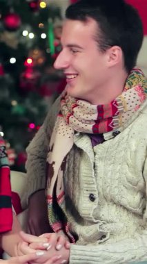 Sıcak, Noel dekore edilmiş bir odada, sıcak süveter ve renkli eşarplar giyen büyüleyici bir çift, sevgi saçan içten hediyeler vererek hoş bir anı paylaşıyorlar. Işıldayan gülümsemeleri ve şefkatli bakışları büyülü bir atmosfer yaratarak,