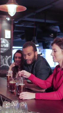 Yetenekli bir barmenin genç yetişkinlerden oluşan neşeli bir gruba soğuk bira servisi yaptığı hareketli bir sahne sergileniyor. Aralarında iki gülümseyen kadın ve bir erkek de yer alıyor. Atmosfer kahkaha ve heyecanla uğulduyor.