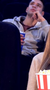 Neşeli, genç, beyaz bir kadın bir anlık mutluluğun tadını çıkarıyor. Patlamış mısırı nazikçe ağzına alıyor ve sinematik sihre daldırıyor. Etrafı canlı izleyicilerle çevrili, neşeli ifadesi heyecan ve beklenti yayıyor, heyecanı somutlaştırıyor.