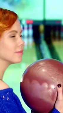 Neşeli, kızıl saçlı, neşeli beyaz bir kızın canlı bir yakın çekimi. Güçlü atışını serbest bırakmaya hazırlanırken kendine güvenen bir bowling topunu tutuyor. Işıl ışıl gülüşü ve ışıl ışıl gözleri oyunun heyecanını yansıtıyor.