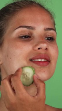 Işıl ışıl gülümseyen genç bir kadın yüzüne serin bir salatalık dilimini nazikçe masaj yapar, canlı yeşil bir krom anahtarla. Bu gençleştirici cilt temizleme ritüeli güzellik ve sağlığın özünü yansıtıyor.