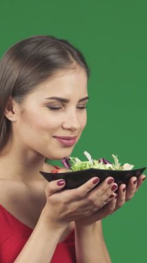 Uzun, dalgalı saçları olan ışıl ışıl bir kadın, parlak siyah bir kasede zarif bir şekilde tutulan renkli bir salatanın çekici kokusunu içine çekerken mutlulukla gülümsüyor. Bu canlı an neşe ve refahın özünü özetliyor, güzelliği kutluyor.