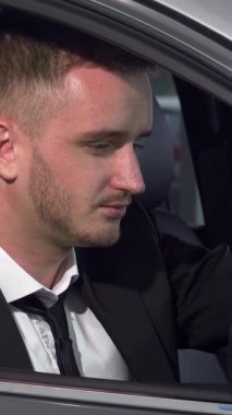 Kendine güvenen genç bir işadamı, şık bir takım elbise giymiş, şık, modern bir arabanın içinden kameraya ışıldıyor. Bu çarpıcı görüntü lüks ve hırsı temsil ediyor, izleyicileri yeni otomotiv maceralarının heyecanını hayal etmeye davet ediyor.