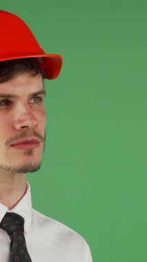 Yakışıklı bir genç adam portresi, bakımlı sakallı, parlak turuncu bir şapka takıyor ve beyaz bir gömlek giyiyor, düşünceli bir şekilde uzaktan bakıyor. Onun düşünceli ifadesi, canlı yeşil renkli bir arka plan üzerine kuruludur.