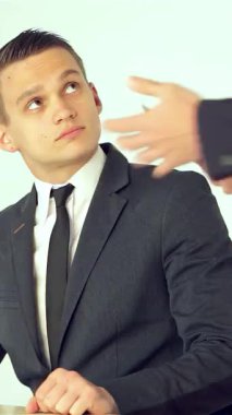 Gösterişli, modern bir ofiste, parlak bir masada oturan genç bir işadamı ayakta duran muadili ile sıkı bir tokalaşmaya girerken kendine güvenen bir ifadeyle yukarı bakıyor. Atmosfer profesyonellik ve karşılıklı saygı gösteriyor.