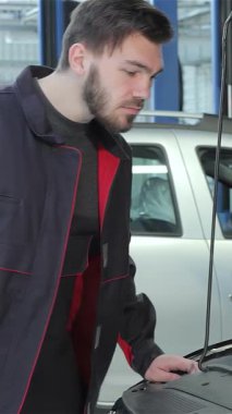 Kendini adamış, bakımlı sakallı ve esmer saçlı genç bir tamirci araba motorunun üzerine eğilip otomotiv tamirindeki uzmanlığını sergiliyor. Profesyonel tulumlar giymiş, motor parçalarını ustalıkla inceliyor.