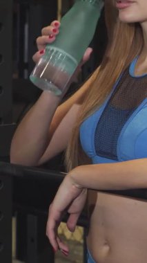 Dinamik bir kesim sahnesinde formda mavi spor bluzlu bir kadın canlandırıcı bir egzersizden sonra suyunu yudumluyor. Kasları ve kendine güveni başkalarını motive eden canlı bir formda yaşam tarzını somutlaştırarak güç ve kararlılık yayıyor.