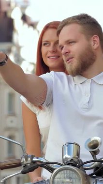 Neşeli genç bir çift hareketli şehirde scooter 'a binerken, erkek büyüleyici bir manzarayı işaret ederken kadın onun kucağına sarılmış olarak neşeyle ışıldıyor. Bu canlı şehir manzarası macera ve romantizm saçıyor.