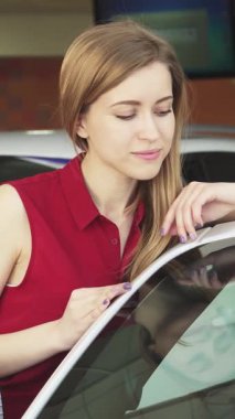 Şık kırmızı bir bluz giyen ışıldayan genç bir kadın galeride yeni üstü açık arabasıyla coşkuyla poz veriyor. Heyecan ve güven saçıyor. Bu canlı sahne, arka planda geçen rüya bir araba satın almanın heyecanını özetliyor.