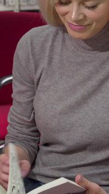 Göz kamaştırıcı sarı saçlı bir kadın, canlı bir üniversite kütüphanesindeki bir kitaba dalmış kameraya gülümserken neşe saçıyor. Sıcak kırmızı sandalyeler ve bilgelikle dolup taşan raflarla çevrili bu sahne çok güzel.