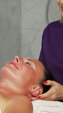 Huzurlu bir kaplıca vahasında, yetenekli bir kadın terapist mutluluğu gözleri kapalı ve huzurlu bir gülümsemeyle yayan mutlu müşterisinin kafasına nazikçe masaj yapar. Yumuşak ışıklandırma ve sakinleştirici renkler sahneyi kaplıyor.