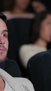 Yoğun gözleri olan odaklanmış genç bir adam, lüks bir sinema koltuğunda oturur, tamamen büyük ekrandaki sürükleyici hikayeye dalmıştır. Yakınlardaki arkadaşlar patlamış mısır ve gazozu paylaşıyor, havayı kahkaha ve heyecanla dolduruyor, canlı bir atmosfer yaratıyor.