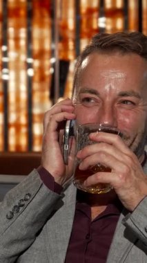 Parlak gri takım elbiseli neşeli bir işadamı bir bardak viskiden zevk alır ve akıllı telefonuyla sohbet eder. Parlak gülüşü ve kahkahası lüks bir barda yankılanıyor, kutlama ve başarının özünü yakalıyor.